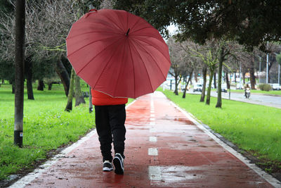 Woman with umbrella walking on wet footpath during rainy season