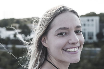 Close-up portrait of smiling young woman with blond hair against sky