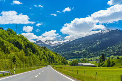 Road amidst green landscape and mountains against sky