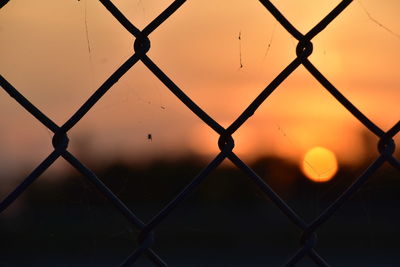 Close-up of chainlink fence against sky during sunset
