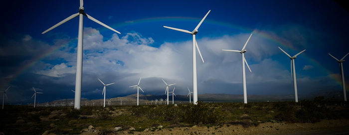 Windmills in field with rainbow against sky