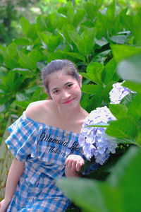 Portrait of young woman standing by flowering plant