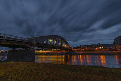 Illuminated bridge over river against sky at night