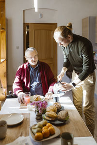 Young man pouring coffee for retired senior father with disability during breakfast at home