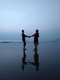 Friends holding hands while standing at beach against sky