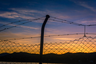 Silhouette barbed wire fence against sky during sunset