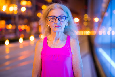 Portrait of woman standing against illuminated city at night