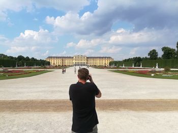 Rear view of man on walkway leading towards castle against cloudy sky