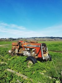 Abandoned tractor on agricultural landscape against blue sky