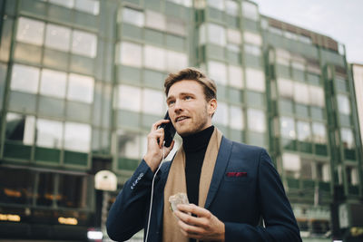 Confident businessman with wrap sandwich talking through smart phone while standing in city