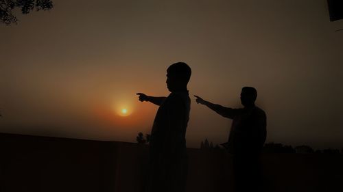 Silhouette men standing against sky during sunset