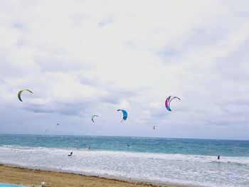 People kiteboarding in sea against cloudy sky