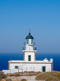 Lighthouse by sea against buildings against clear blue sky