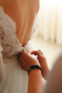 Cropped hands of woman dressing up bride at home