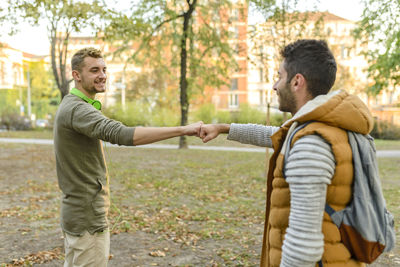 Young friends bumping fist in park during autumn