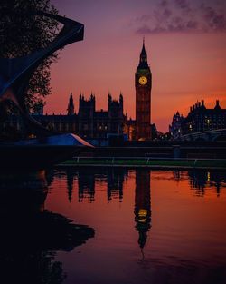 Reflection of big ben in river against orange sky at dusk