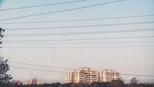 Low angle view of power lines against buildings in city