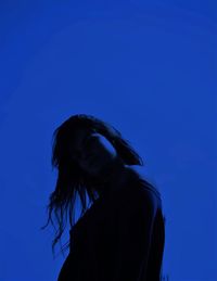 Low angle portrait of woman standing against blue sky