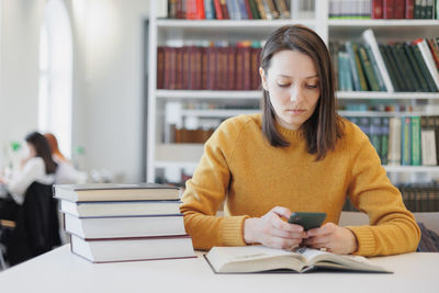 Young woman using mobile phone while sitting on table