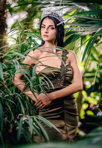 Portrait of beautiful bride wearing crown while standing amidst plants at botanical garden