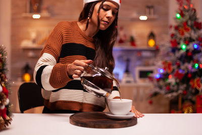 Young woman pouring tea at home during christmas