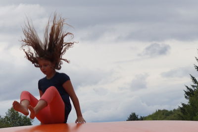 Young woman against trees against sky