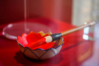 Close-up of paintbrush on red watercolor paint filled bowl