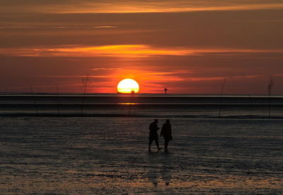 Silhouette people on beach against sky during sunset