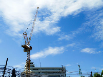 Low angle view of cranes at construction site against sky
