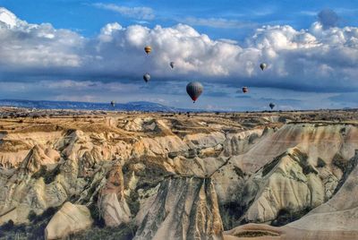 Hot air balloons flying over rock formation against sky