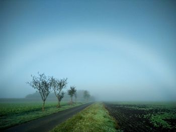 Road amidst field against sky during foggy weather