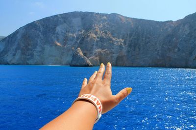 Close-up of hand reaching towards sea against mountain