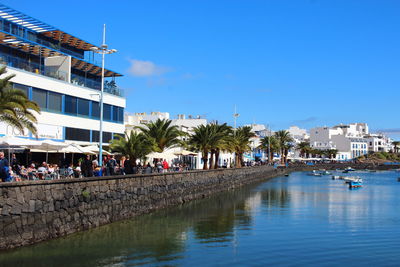 Buildings by river against clear blue sky