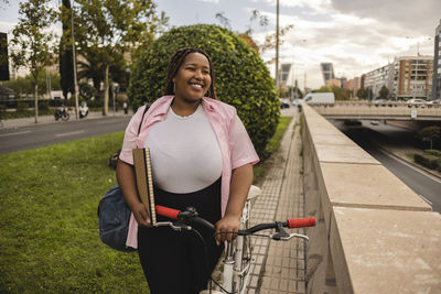 Happy young woman standing with bicycle at footpath
