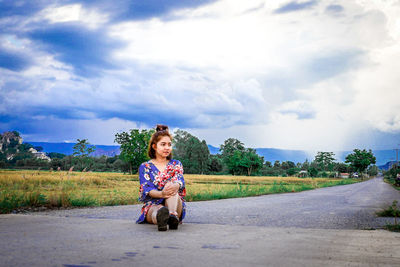 Portrait of woman sitting on road against sky