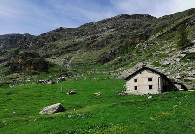 House on field by mountain against sky