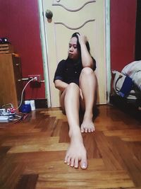 Young woman sitting on hardwood floor at home