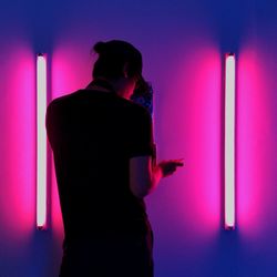 Rear view of man silhouette standing against illuminated wall