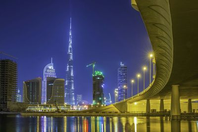 Low angle view of illuminated burj khalifa in front of river in city at night