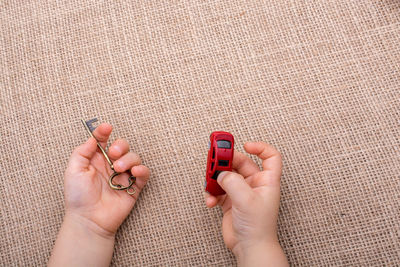 Cropped hands of child holding toy car and key on burlap