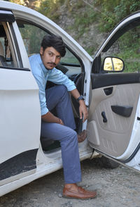 A handsome young indian guy looking sideways while sitting in the car with open door 