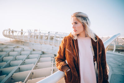 Young woman standing on railing against clear sky