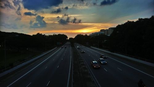 Vehicles on highway against sky during sunset