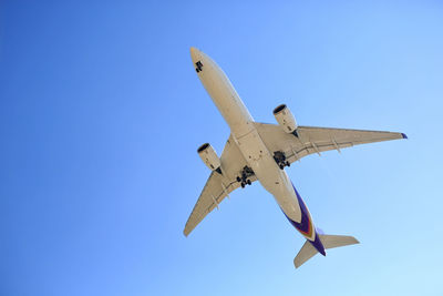 Low angle view of airplane flying against clear blue sky