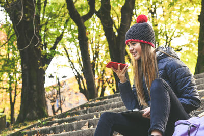 Girl with wool cap sitting in the park using smartphone. teen use mobile phone, doing vocal messages