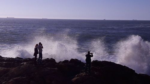 People standing on rock by sea against clear sky