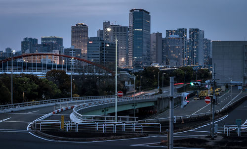 Vehicles on road by illuminated buildings against sky in city