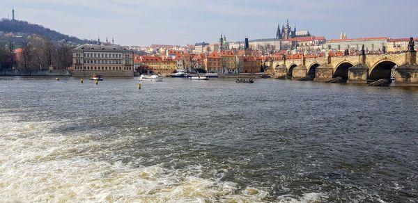 Bridge over river by buildings in city against sky