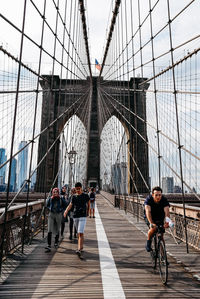 People on footbridge against bridge in city