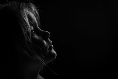 Close-up of girl looking away against black background